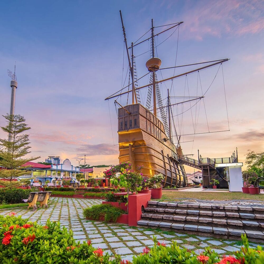 Replica of Portuguese ship at Malacca Maritime Museum, a top attraction on Malacca tour from Kuala Lumpur, with flowers and sunset sky."