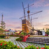 Replica of Portuguese ship at Malacca Maritime Museum, a top attraction on Malacca tour from Kuala Lumpur, with flowers and sunset sky."