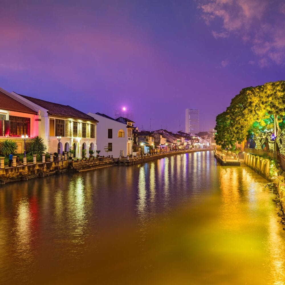 Scenic night view of Malacca River with colorful lights and heritage buildings, a popular stop on a Malacca tour from Kuala Lumpur.
