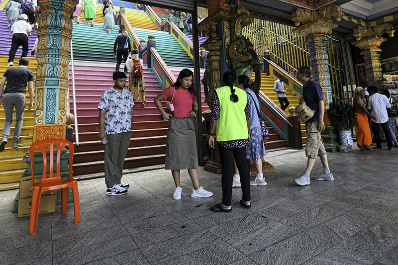 Tourists being stopped at Batu Caves entrance for not following the batu caves dress code, with temple staff advising on proper attire before climbing the colorful staircase.
