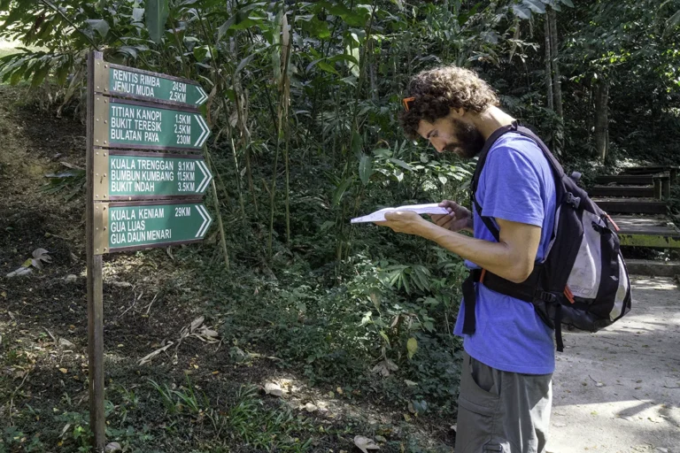Tourist looking at a map near trail signpost showing things to do in Taman Negara Pahang