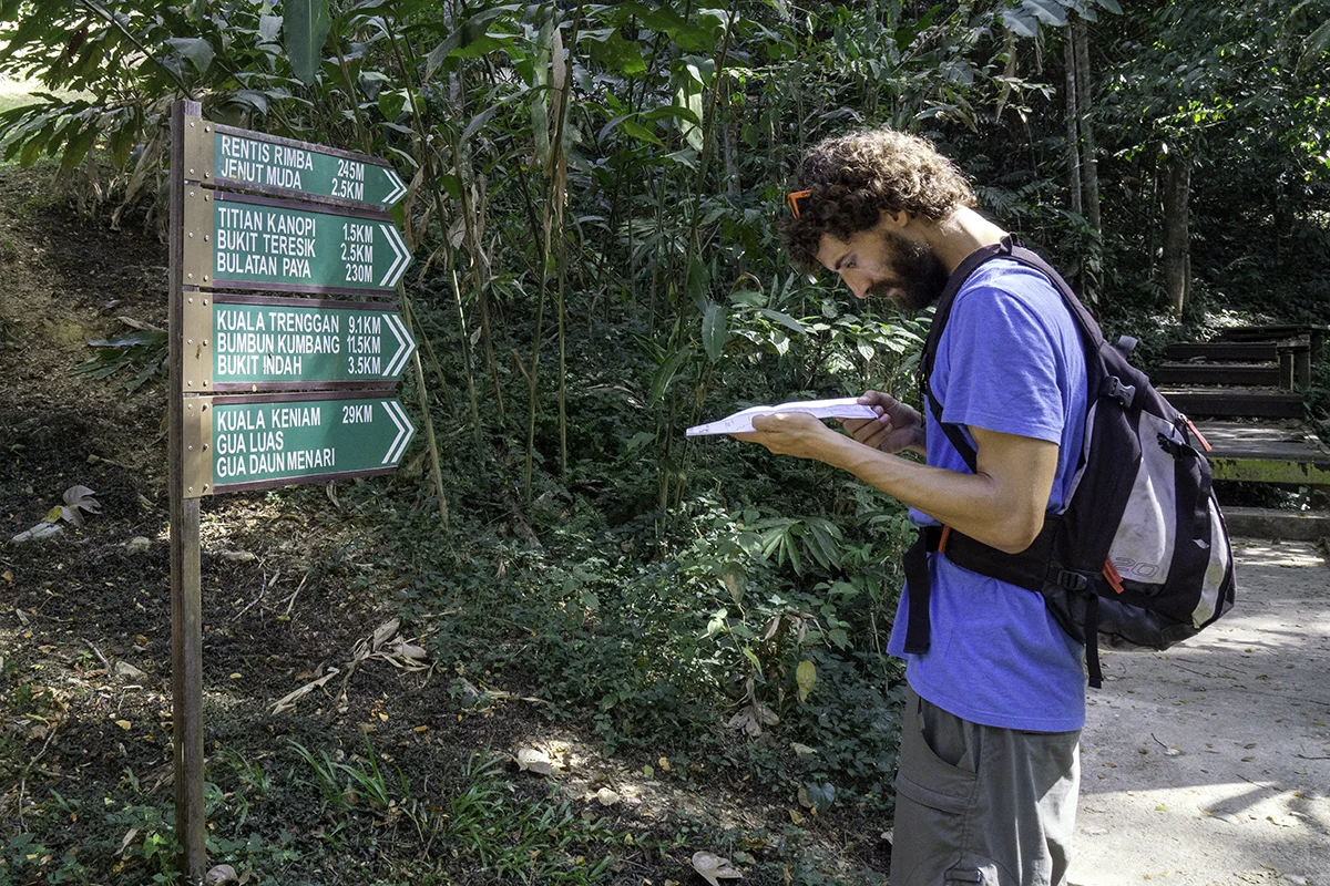 Tourist looking at a map near trail signpost showing things to do in Taman Negara Pahang
