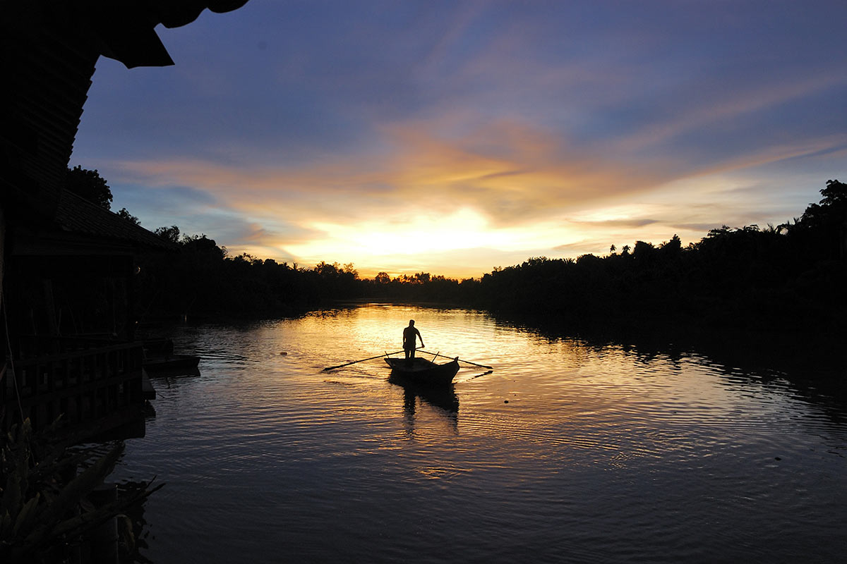 Silhouette of a boatman rowing a sampan at Kampung Kuantan Fireflies Park during sunset