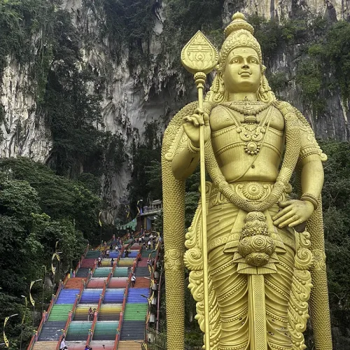 Batu Caves Visit – Free Stop with Malaysia Elephant Sanctuary Tour Golden Lord Murugan statue and rainbow steps at Batu Caves, a free stop included with the Malaysia Elephant Sanctuary tour from Kuala Lumpur.