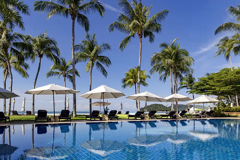 Luxury beachfront hotel in Langkawi with poolside loungers and palm trees.