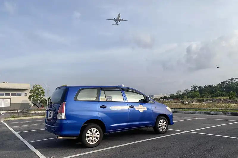 Blue executive airport taxi at Kuala Lumpur International Airport with airplane flying above