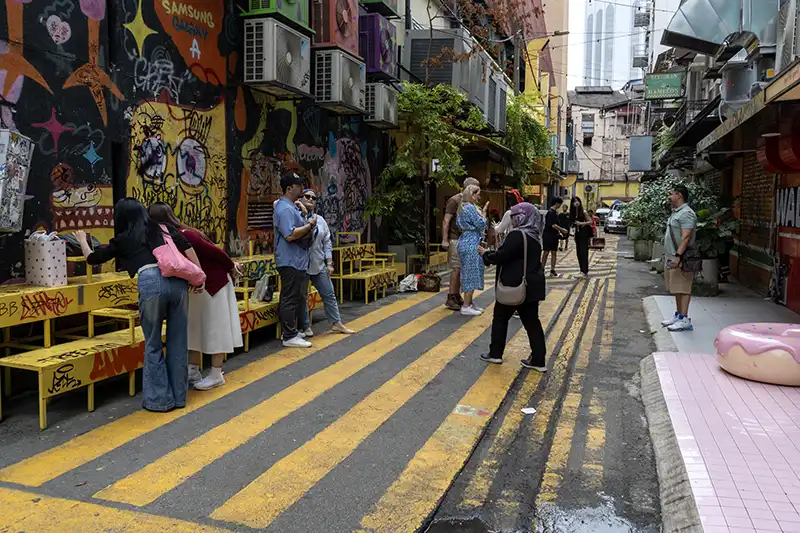 Tourists walking through Kwai Chai Hong in Chinatown Kuala Lumpur surrounded by lanterns and heritage murals.