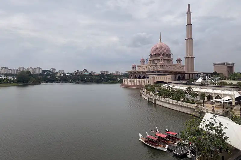 Scenic view of Putra Mosque beside Putrajaya Lake with traditional boats on the water.