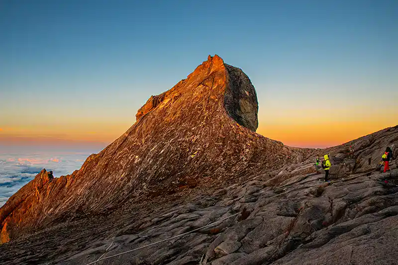 Climbers approaching the rocky summit of Mount Kinabalu at sunrise