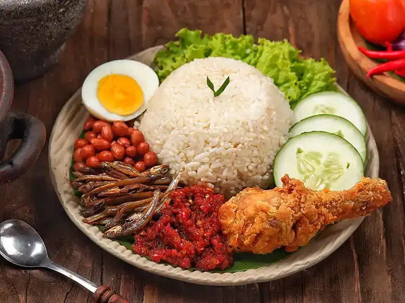 Nasi lemak served with sambal, fried anchovies, peanuts, cucumber and chicken in a traditional Malaysian meal