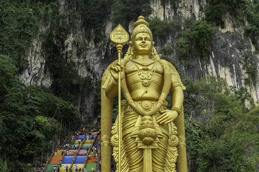 Visitors climbing the 272 rainbow steps at Batu Caves beneath the golden Lord Murugan statue in Selangor
