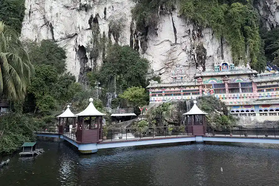 Cave Villa at Batu Caves with a walkway bridge over a pond, colourful Hindu temple facade built into the limestone cliff face