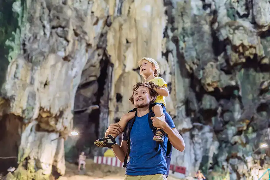 Father carrying child on shoulders inside Batu Caves Temple Cave, exploring the limestone cavern on a family visit