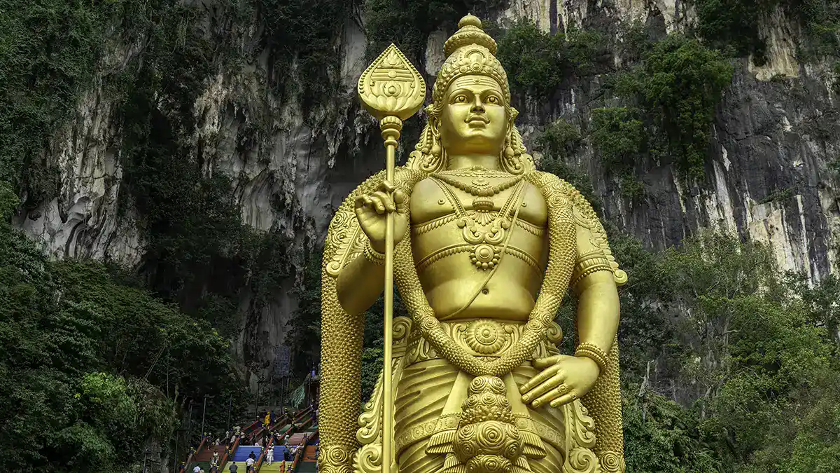 Golden Lord Murugan statue at Batu Caves with the rainbow staircase and limestone cliffs in Selangor near Kuala Lumpur