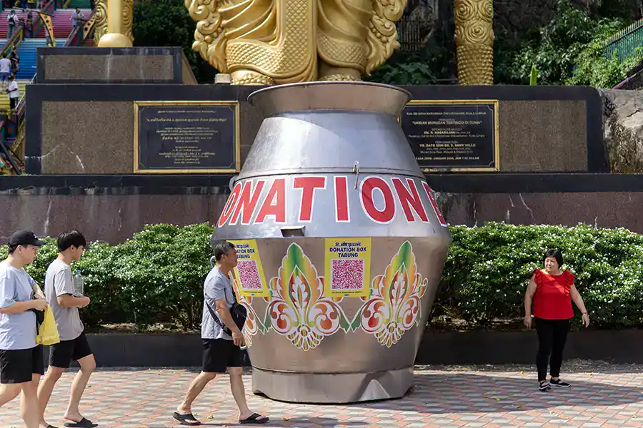 The giant stainless steel donation box at the base of Batu Caves, believed to be the largest in the world, with the Lord Murugan statue and rainbow staircase behind it