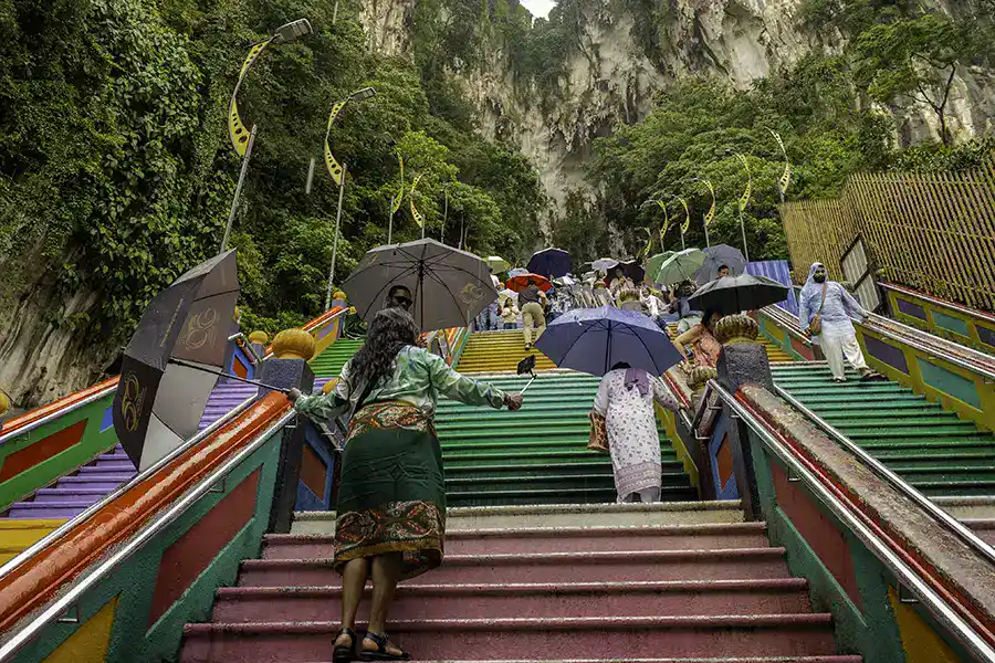 Visitors climbing the Batu Caves rainbow staircase during rainy weather in Kuala Lumpur