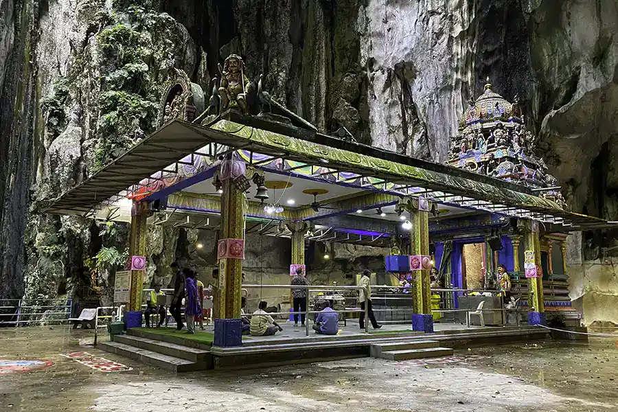 The Hindu shrine inside the Temple Cave at Batu Caves, with ornate gopuram tower and worshippers gathered beneath the towering limestone walls