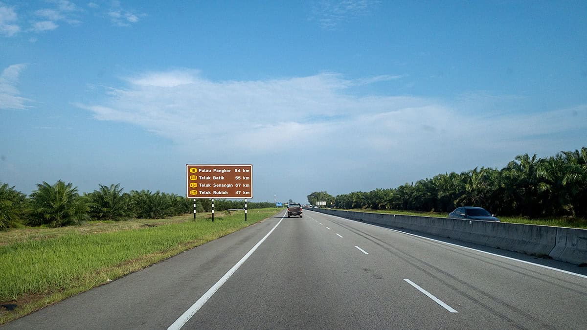 Highway road in Malaysia showing distance signs for Pangkor Island and coastal destinations, representing transport options for getting around Malaysia