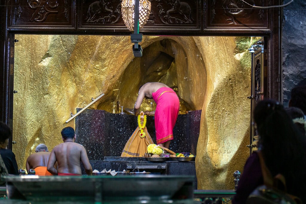 Hindu priest placing a flower garland during a puja ritual inside Batu Caves temple in Kuala Lumpur