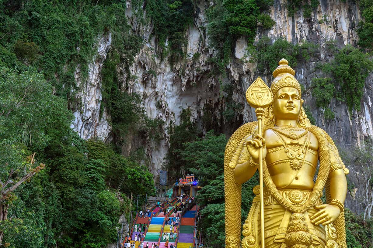 Golden statue of Lord Murugan standing beside the colourful staircase leading to the Cathedral Cave at Batu Caves, Kuala Lumpur