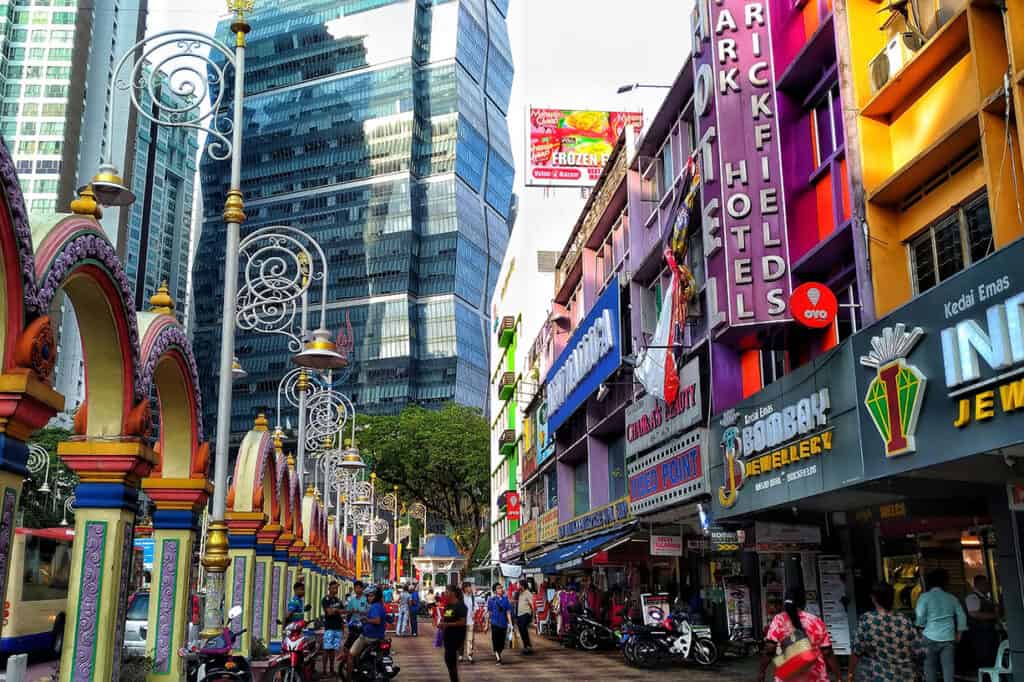 Colourful street in Brickfields Little India with ornate temple arches, gold jewellery shops, and modern towers in the background — things to do in Brickfields Kuala Lumpur for first-time visitors