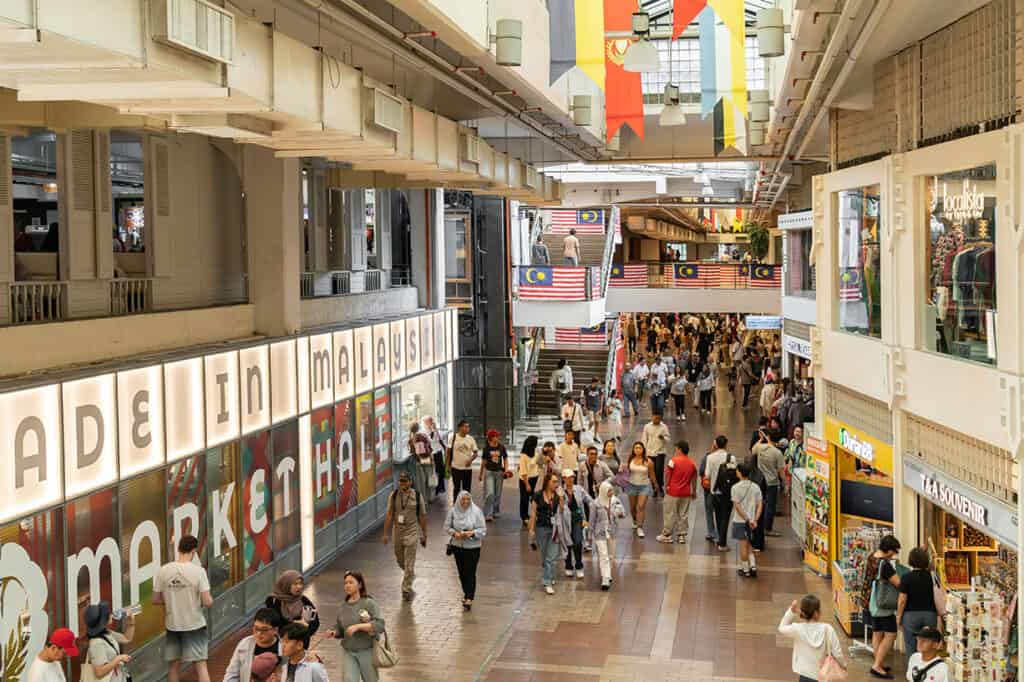 Interior of Central Market Kuala Lumpur showing the Made in Malaysia Market Hall with tourists browsing local craft shops, souvenir stores and Malaysian flags on the staircase