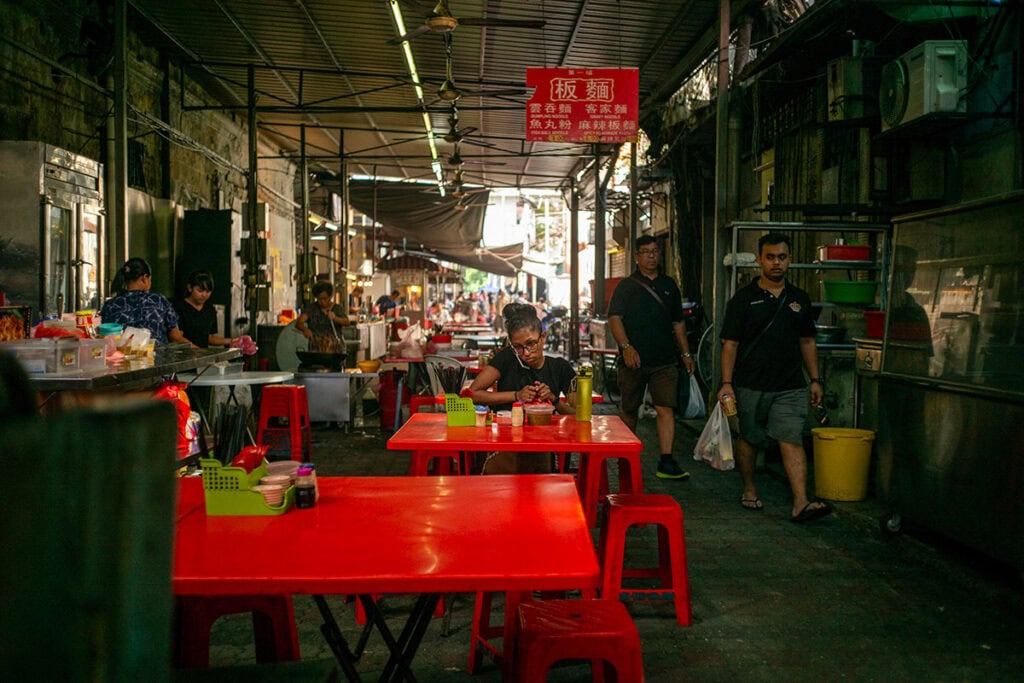 Madras Lane hawker stalls in Chinatown Kuala Lumpur — covered alley with red tables and Chinese noodle signboards