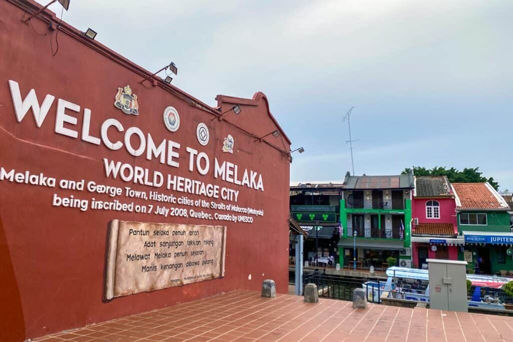 Welcome to Melaka World Heritage City sign on the iconic red colonial wall with colourful Peranakan shophouses alongside the river — a popular day trip destination from Kuala Lumpur