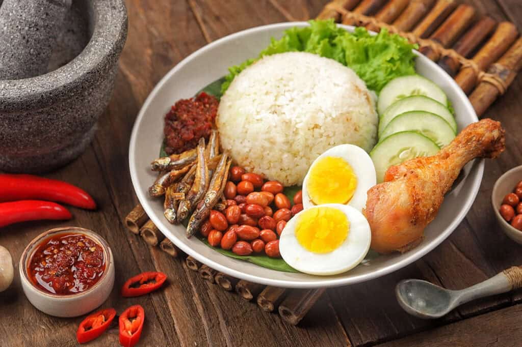 A bowl of Nasi Lemak with coconut rice, sambal, anchovies, peanuts, boiled egg, and fried chicken — Malaysia's national dish and a popular Malaysian food experience in Kuala Lumpur cooking classes