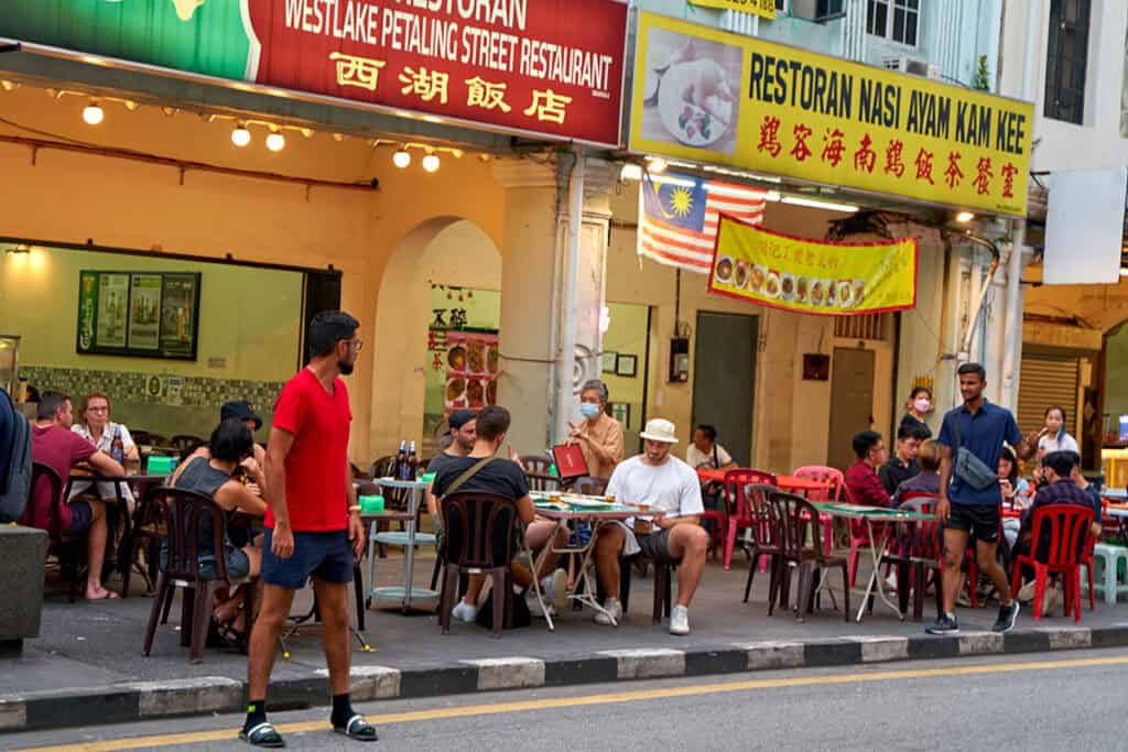 Outdoor dining along Petaling Street in Chinatown 
Kuala Lumpur — tourists and locals eating at pavement 
tables outside heritage shophouses