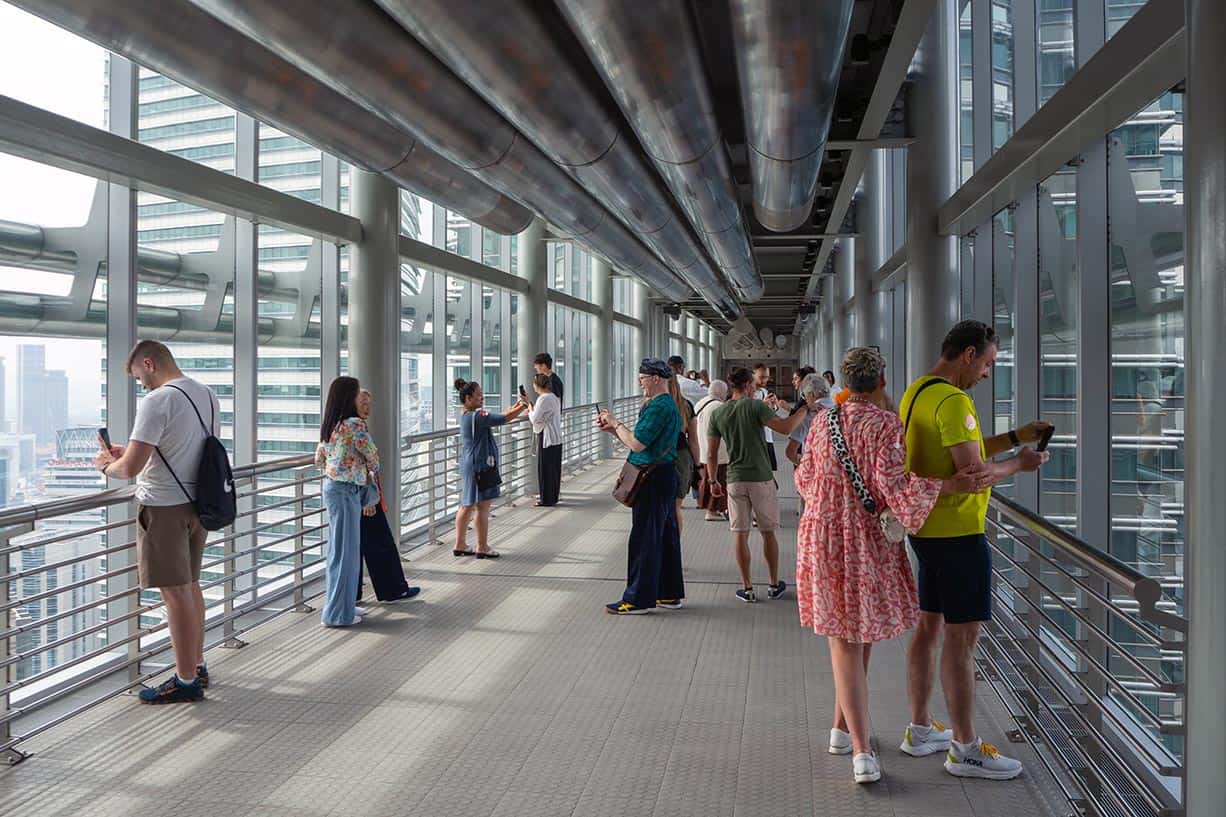 Tourists photographing the Kuala Lumpur skyline from inside the Petronas Twin Towers Skybridge — one of the best things to do in KLCC