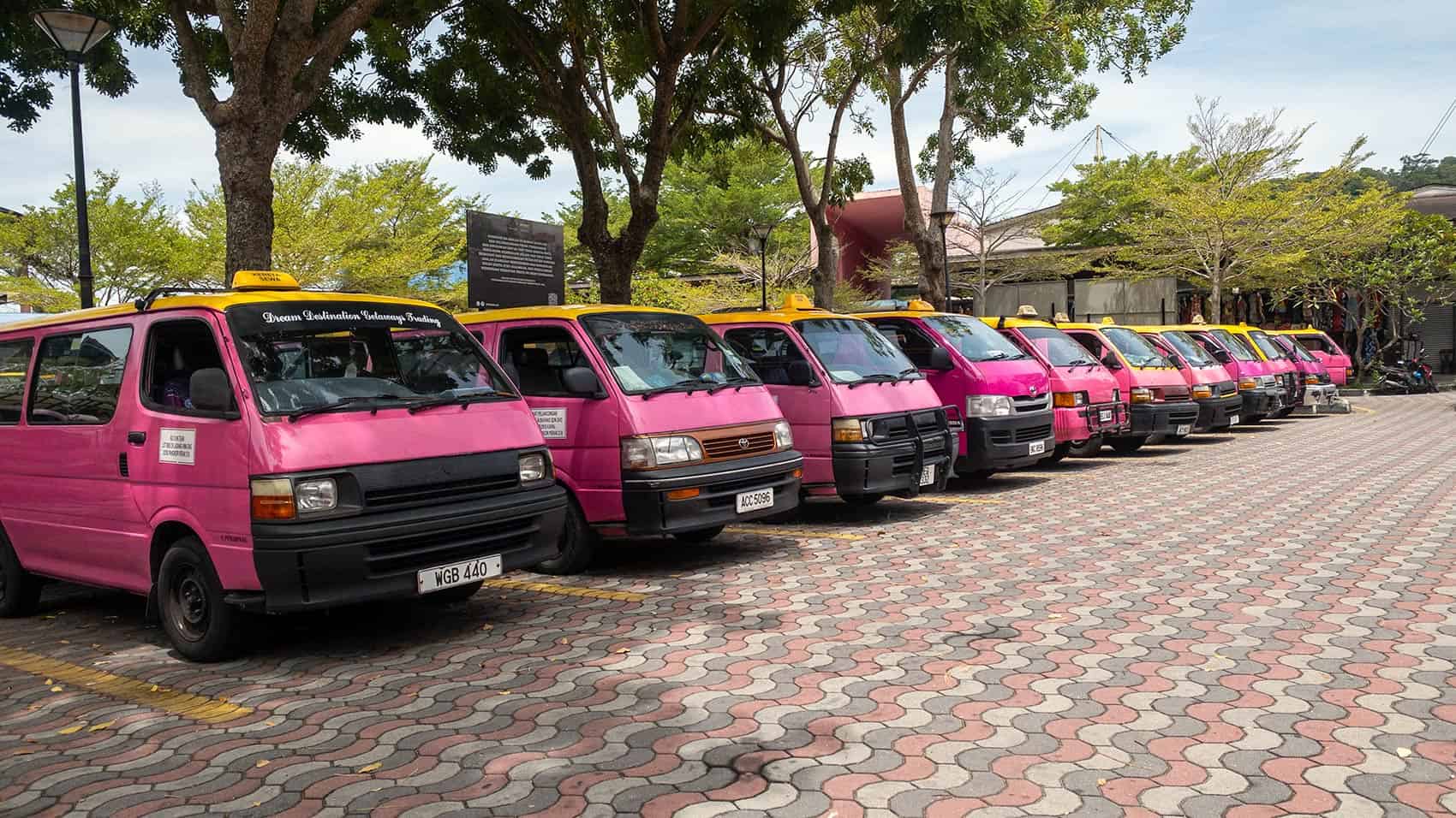 Row of bright pink Toyota taxi vans with yellow rooftop signs lined up at Pangkor Island jetty — the main transport option for getting around Pangkor Island