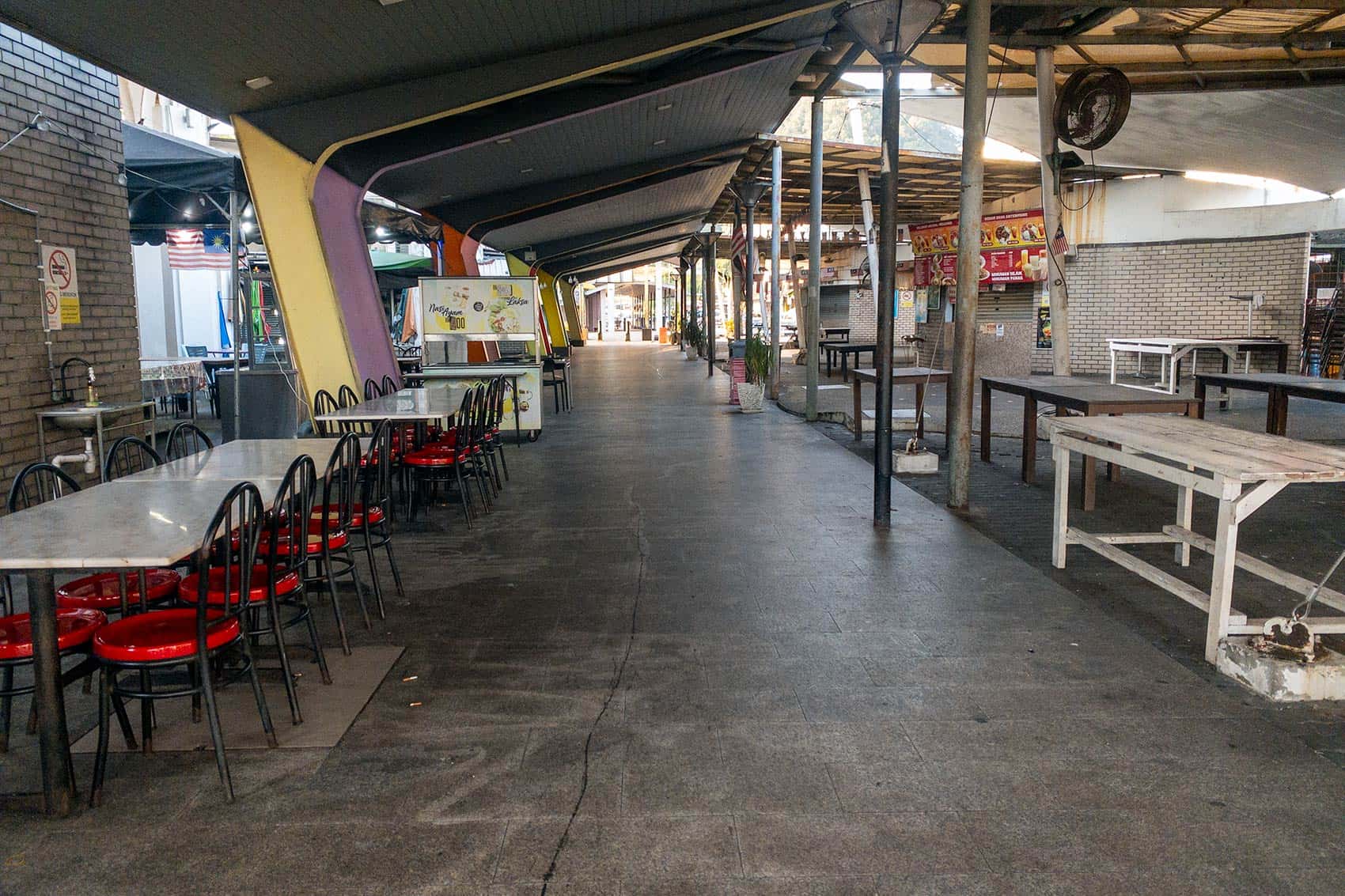 Empty covered hawker stall area adjacent to Lumut Jetty ferry terminal — food stalls closed during editor visit, with tables and chairs unoccupied