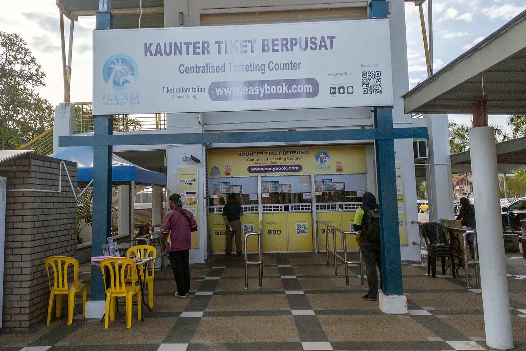 Lumut Jetty centralised ticketing counter showing the Kaunter Tiket Berpusat sign with easybook.com online ticketing and passengers queuing to purchase Pangkor Island ferry tickets