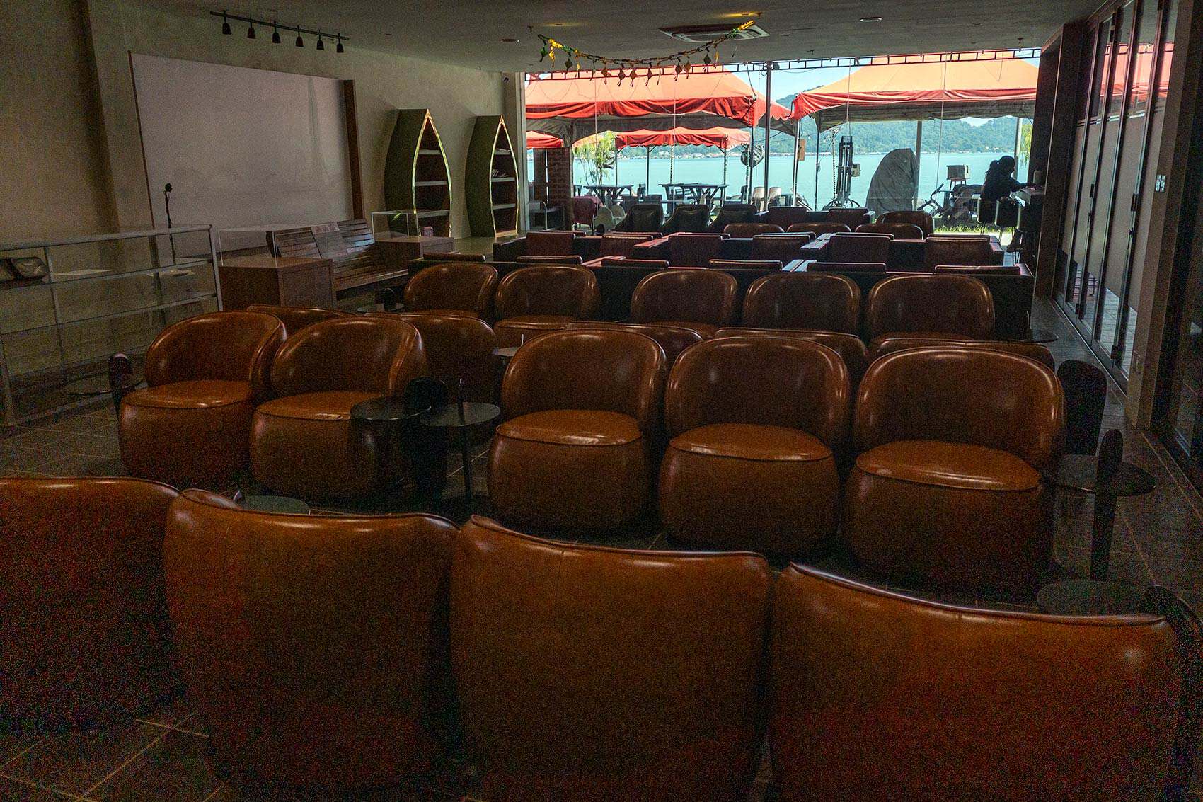 Interior of the Silver Lounge at Marina Island Jetty showing rows of leather armchairs facing the sea view terrace with red parasols and Pangkor Island visible in the background