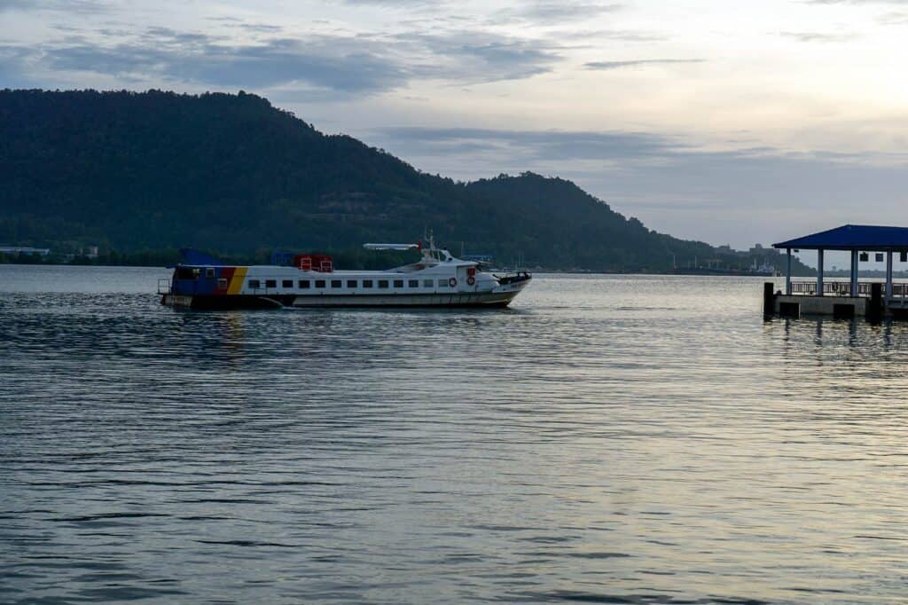 Pangkor Island ferry reversing out from Lumut Jetty at dawn with the island's forested hills visible in the background