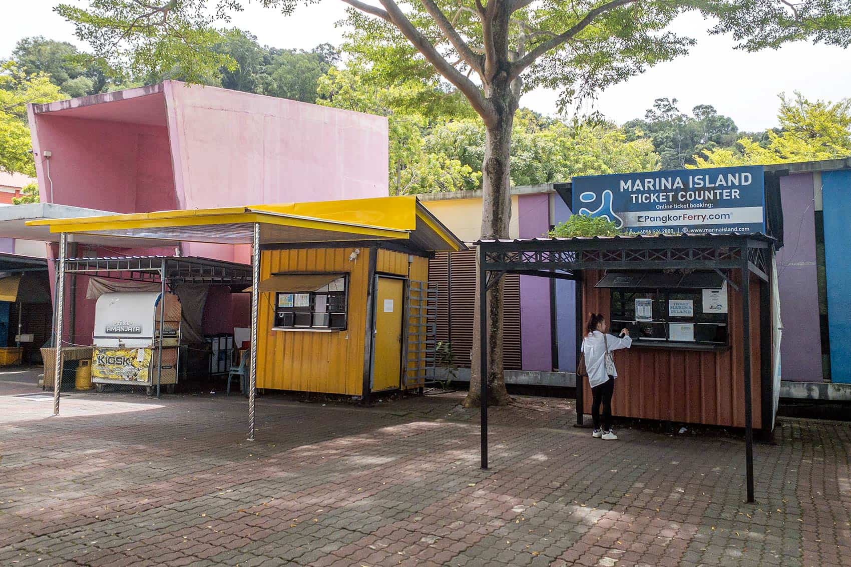 Two ferry ticket counters at Pangkor Island Jetty — yellow counter on the left for Lumut Jetty ferry returns and dark brown Marina Island Ticket Counter on the right for Marina Island Jetty returns