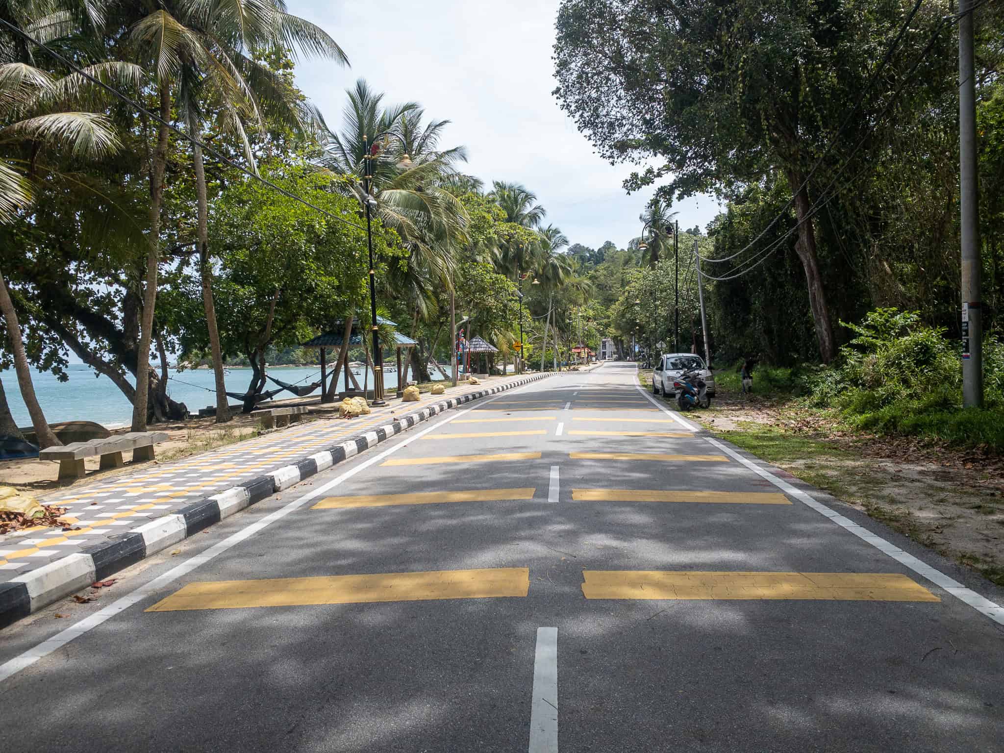 Narrow two-lane beachfront road on Pangkor Island lined with palm trees — typical road conditions on the island where parking is limited during weekends