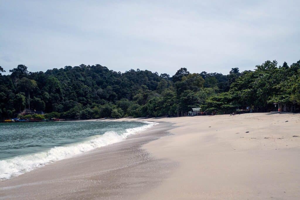 Pantai Pasir Giam on Pangkor Island, a quiet sandy beach backed by forested hills and calm shallow waves.