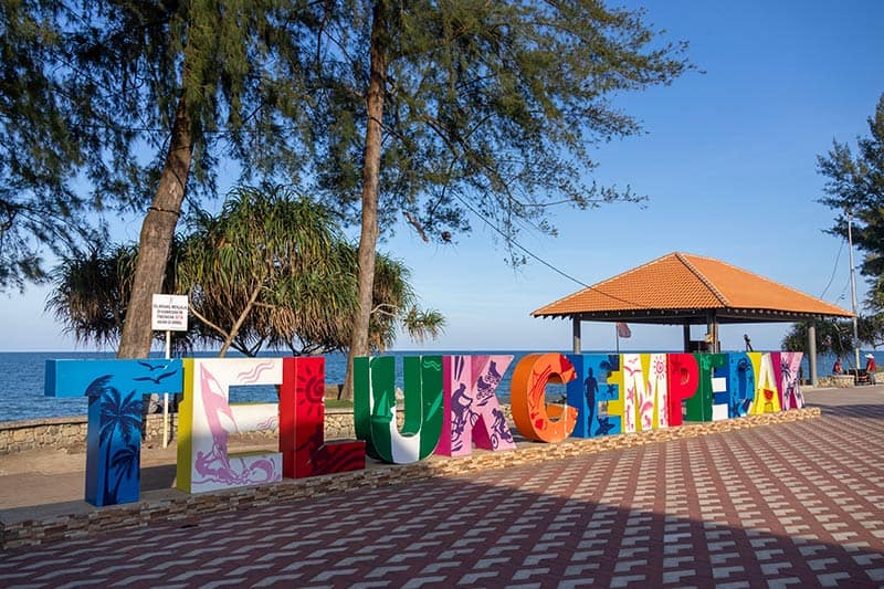 Colourful Teluk Cempedak landmark sign on the beachfront promenade with casuarina trees and the South China Sea in the background, Kuantan, Pahang