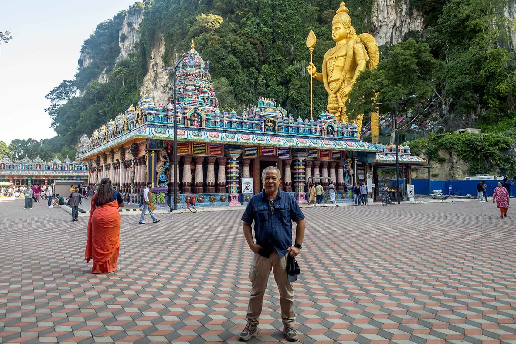 Guide Anuar standing at Batu Caves entrance plaza in front of Sri Subramaniar Swamy Temple with Lord Murugan statue and limestone hill in the background