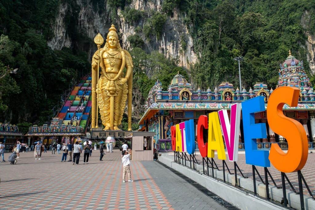 The 42-metre golden Lord Murugan statue at Batu Caves with the rainbow-coloured staircase and Hindu temple in the background — the first stop on a Kuala Lumpur city tour