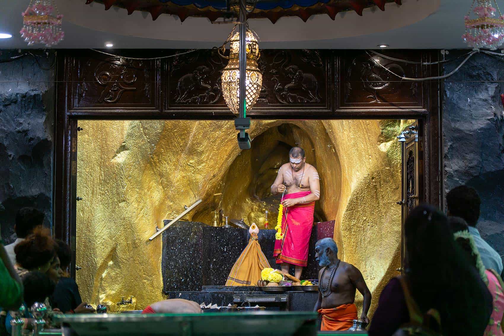 Hindu priest performing puja prayer ceremony inside Batu Caves Temple Cave — worshippers welcome to observe during opening hours