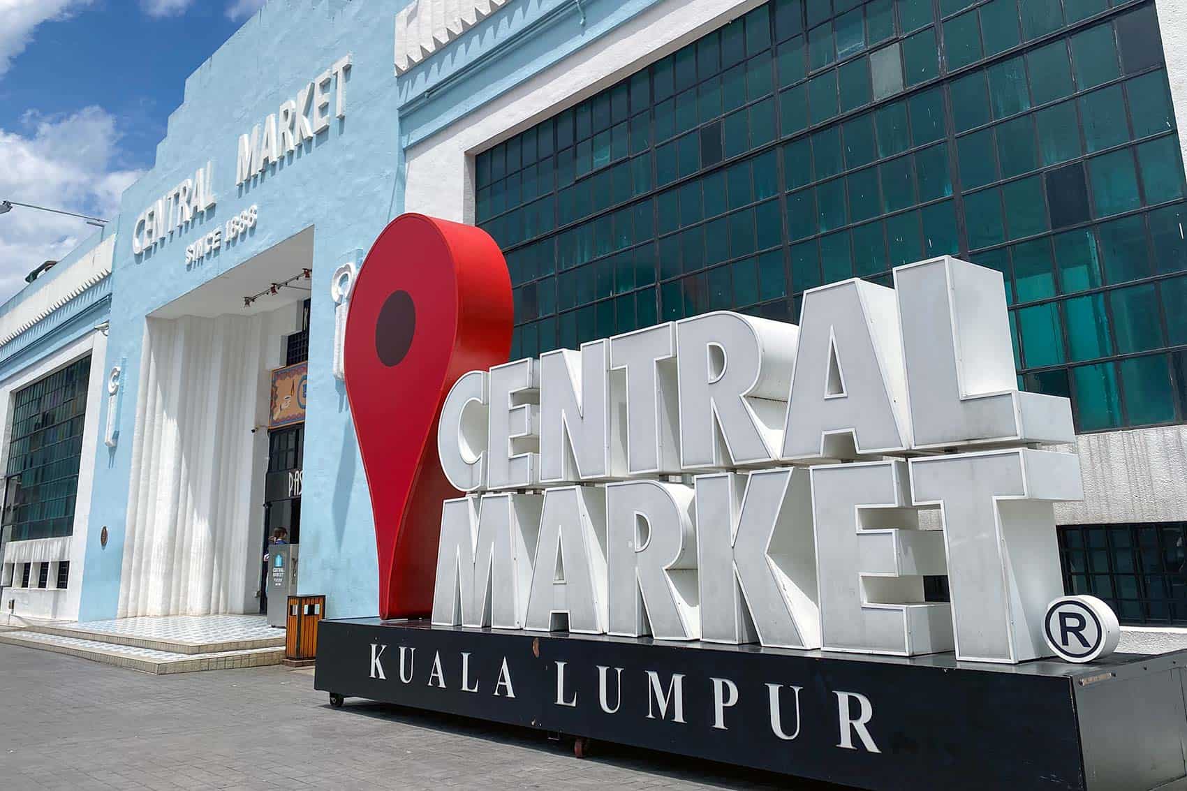 Central Market Kuala Lumpur entrance with the large white letter sign and red map pin sculpture in front of the heritage light-blue Art Deco building
