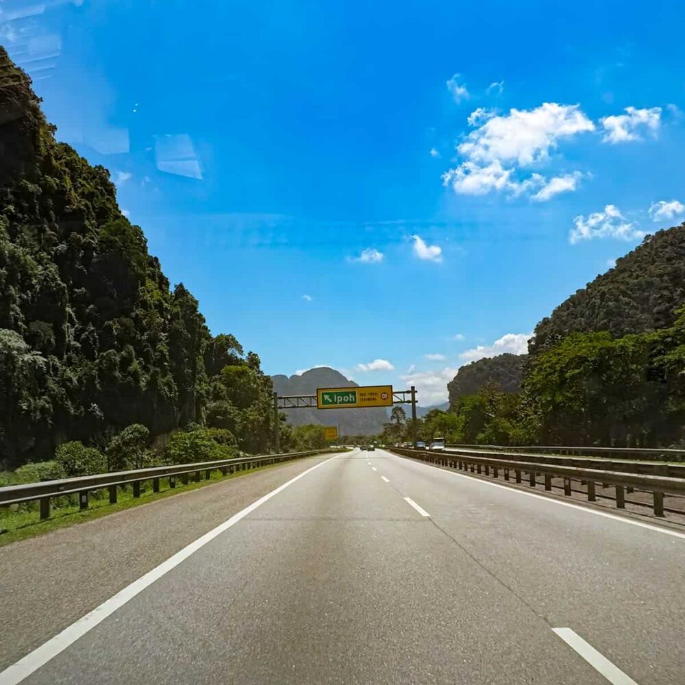 View from inside a private transfer vehicle on the North-South Expressway approaching Ipoh, with the Ipoh highway sign and limestone karst hills visible