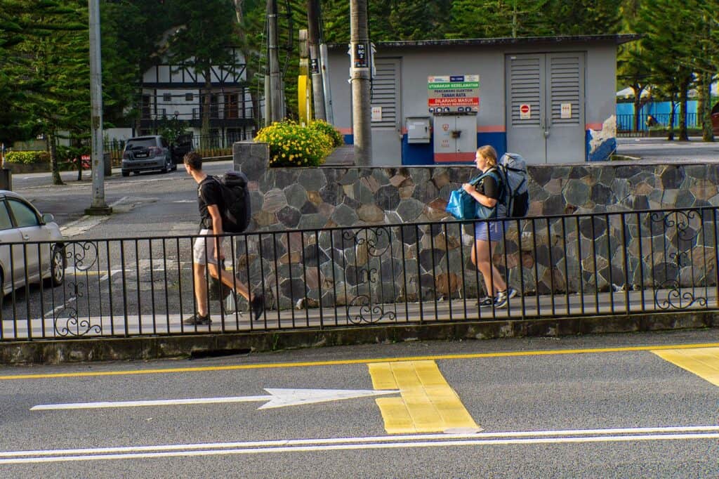 Two backpacker tourists walking along the footpath in Tanah Rata town centre — where to stay at Cameron Highland is best decided by proximity to the bus station and walkable amenities