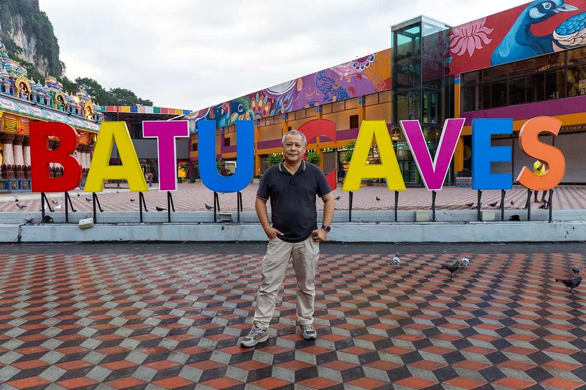 Anuar, Private Tour Specialist based in Kuala Lumpur, standing in front of the colourful Batu Caves sign with the Hindu temple entrance visible behind him