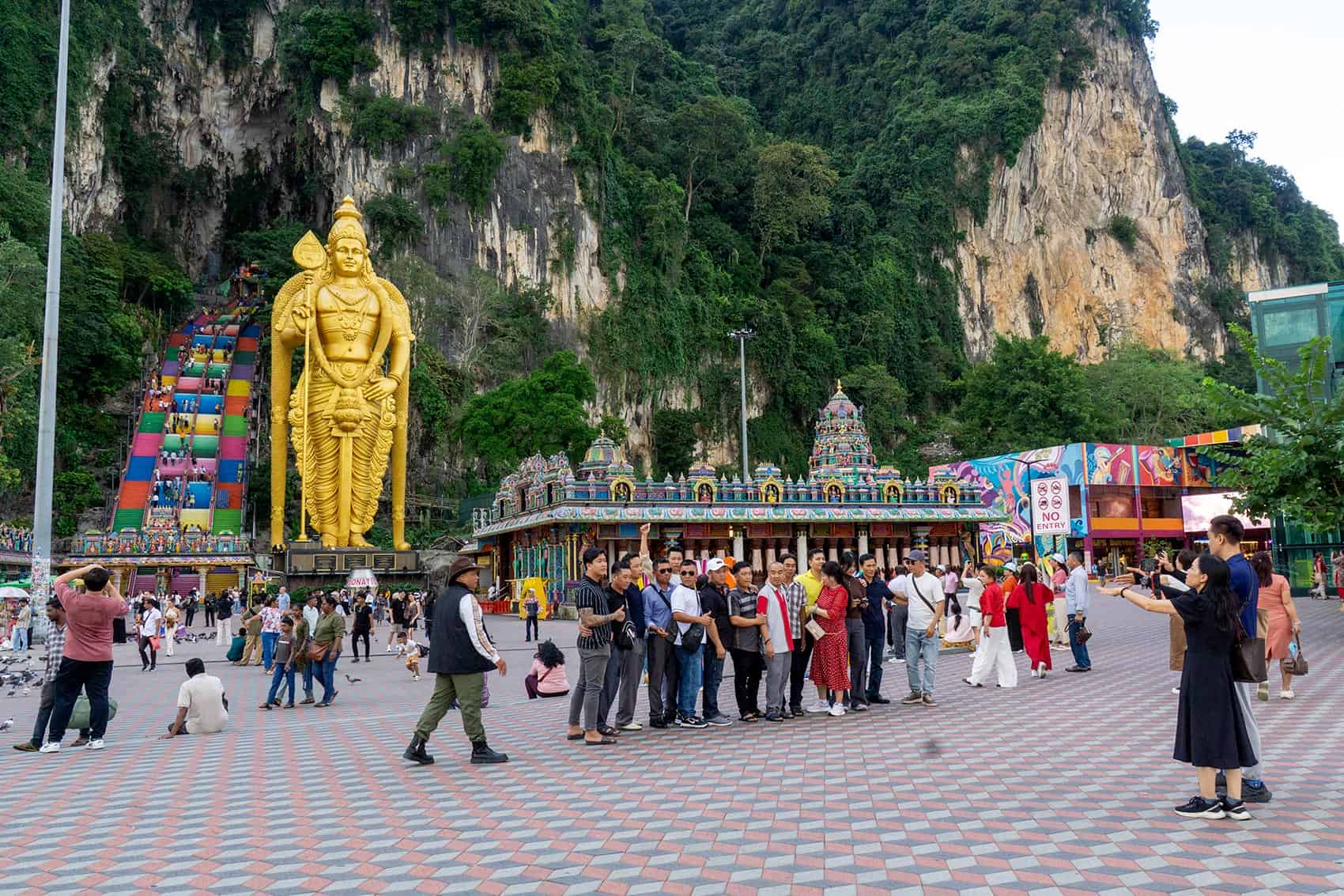 Tourists queuing for photos in front of the Lord Murugan statue at Batu Caves, with the rainbow staircase and temple complex behind