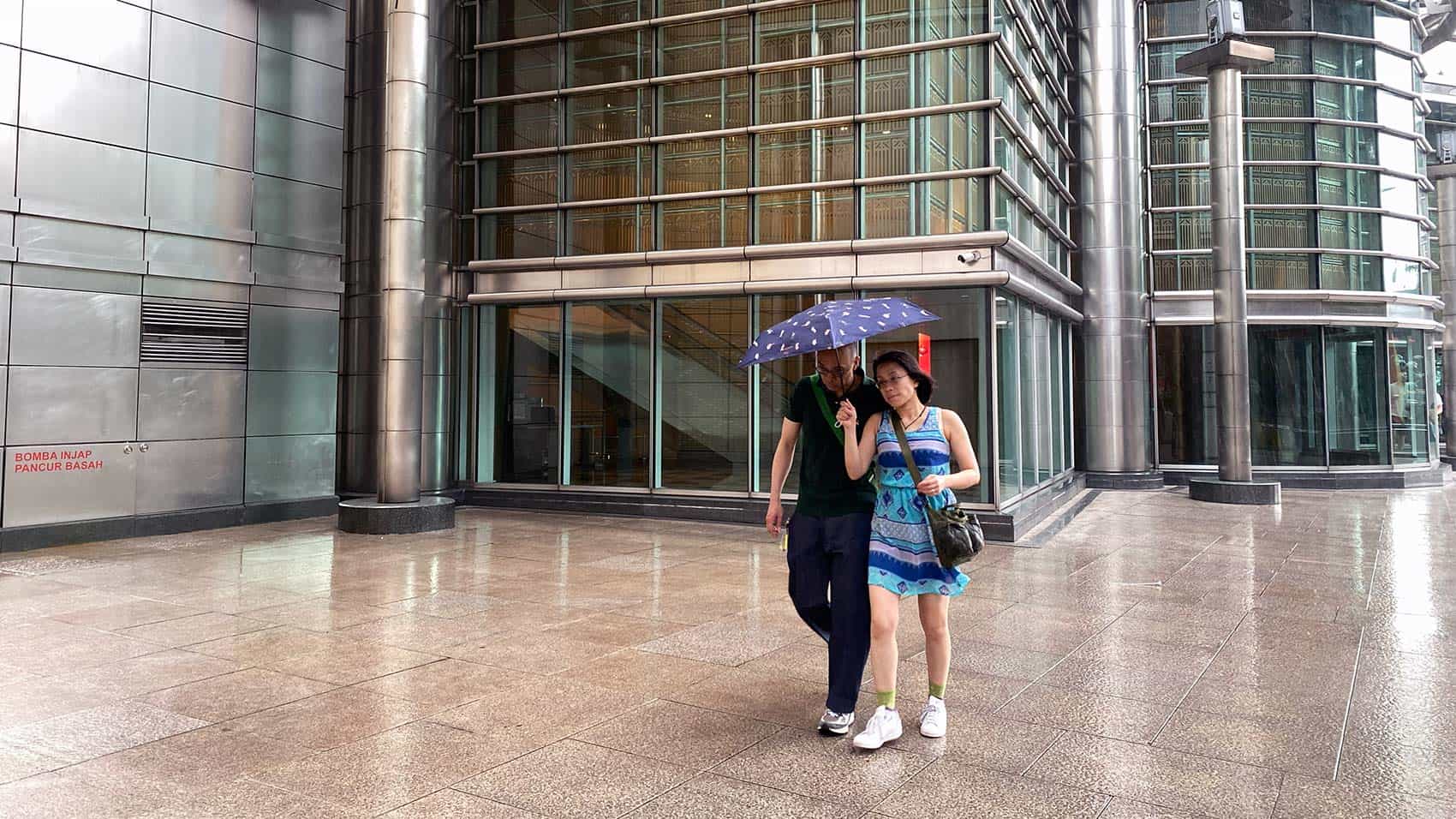 Couple sheltering under an umbrella during a sudden afternoon downpour near Petronas Twin Towers — best time to visit Kuala Lumpur