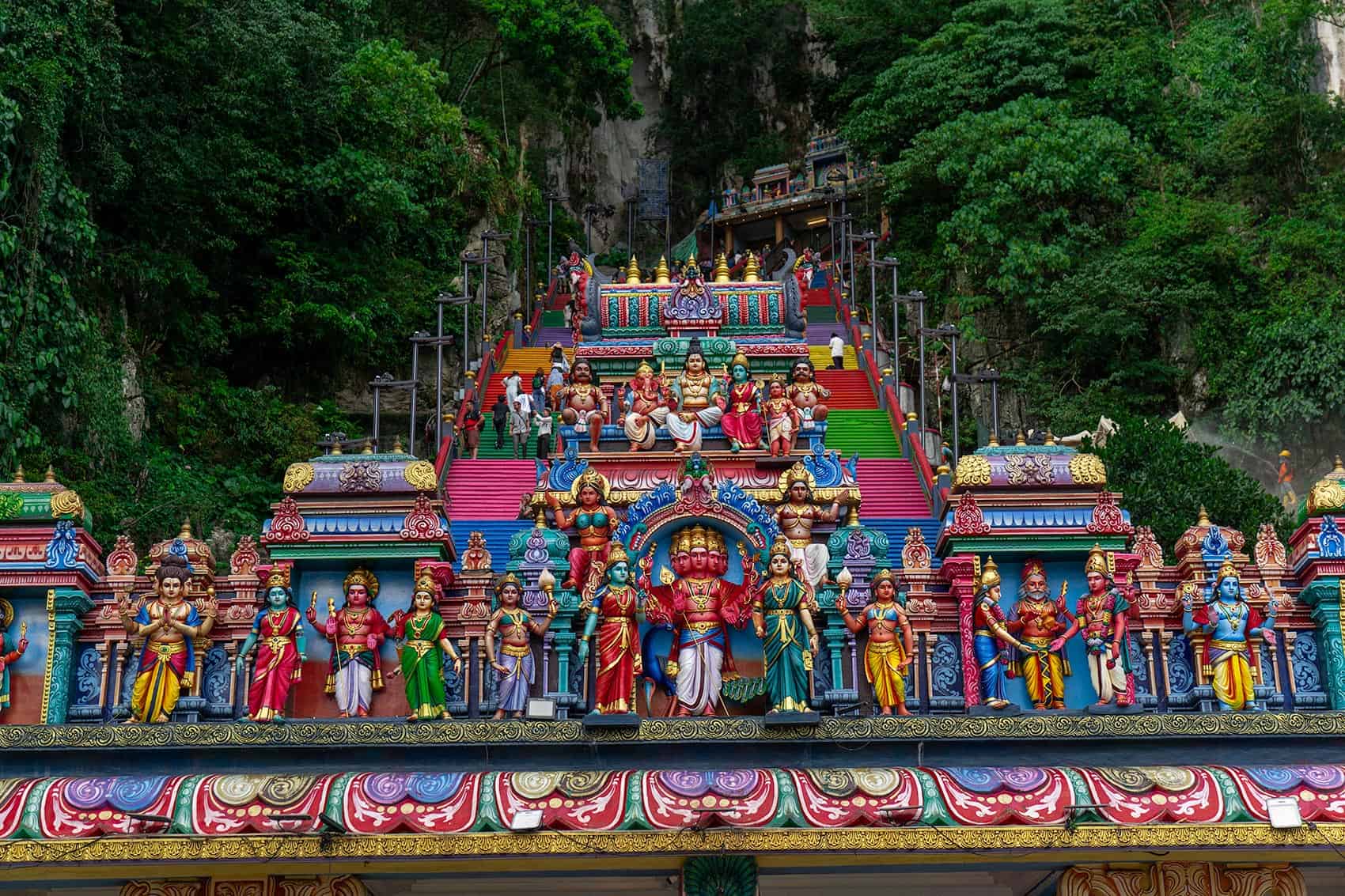 The gopuram archway at the base of the Batu Caves staircase, showing Lord Murugan flanked by his consorts Valli and Deivanai
